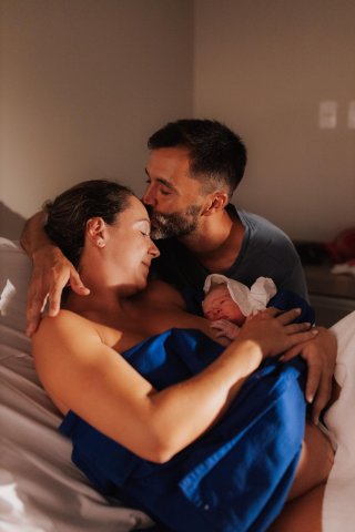 Новые родители обнимают своего новорожденного в мягко освещенной спальне во время тихого момента связи